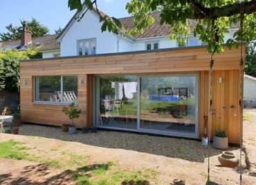 Modern wooden garden room with large glass sliding doors.