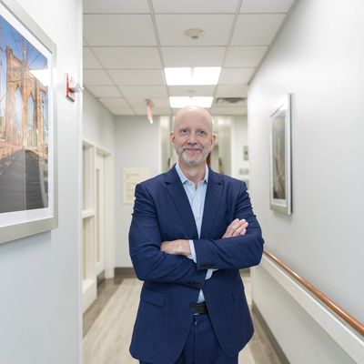 Dr. Miles is smiling while standing in the hospital hallway next to a photo of the Brooklyn Bridge.
