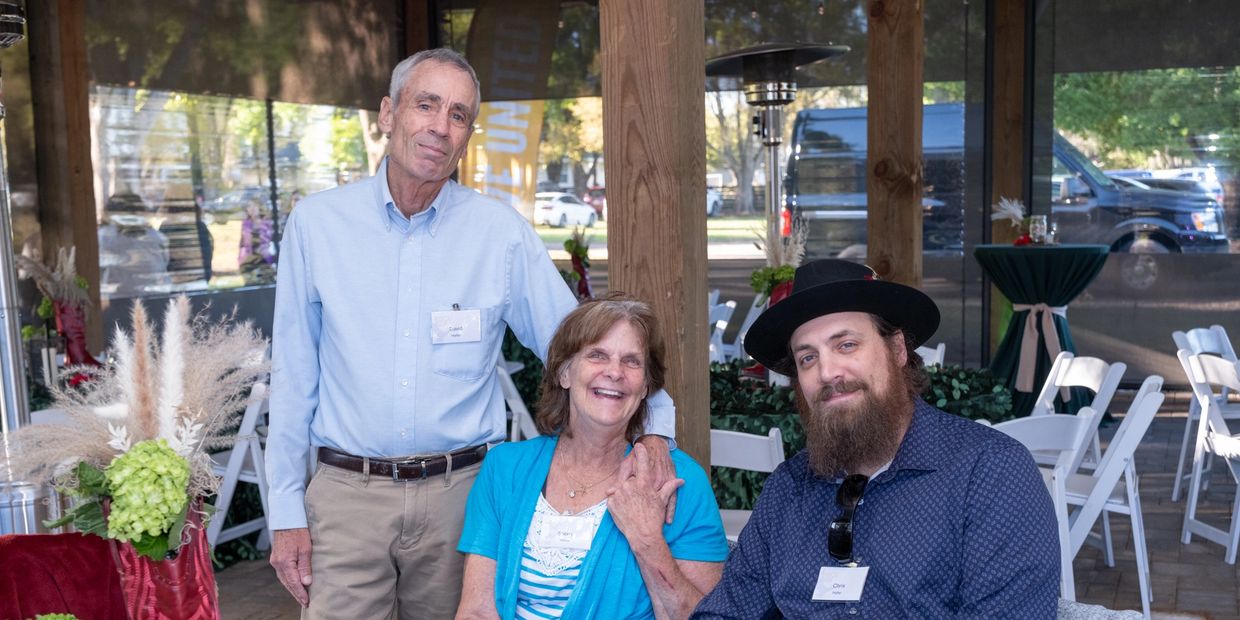 Three people posing together at an outdoor event with name tags.