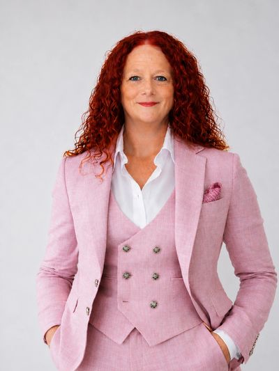 Confident woman in a pink suit with curly red hair.