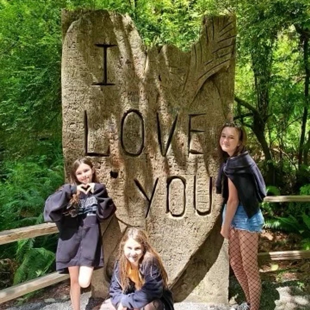 Three girls posing by a large stone carving saying 'I LOVE YOU'.