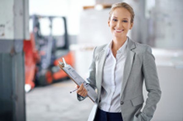 Smiling businesswoman in a warehouse holding a clipboard.
