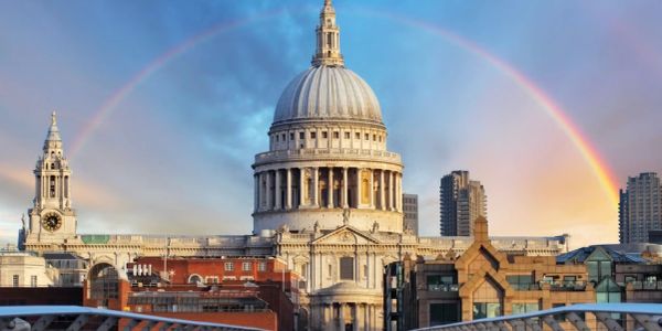 A rainbow arches over a historic domed building in a city.