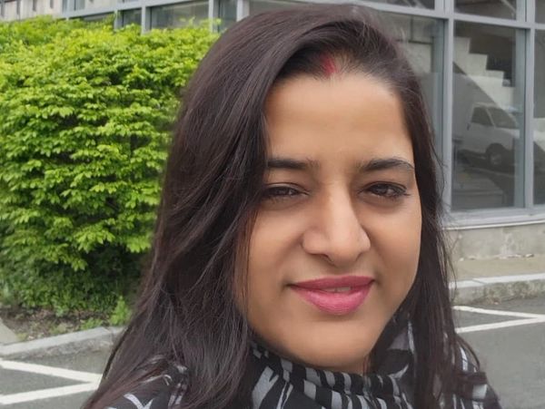 Woman taking a selfie outdoors near a modern glass building and greenery.