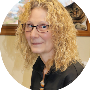 Smiling woman with curly blonde hair and glasses indoors.