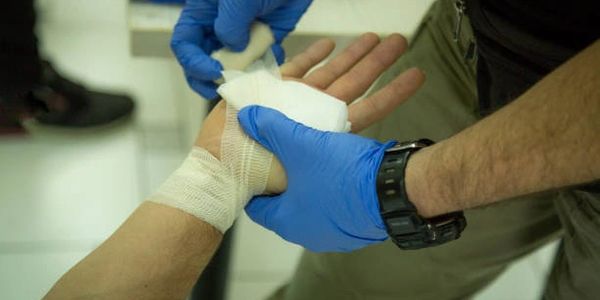 A person wearing gloves bandages another person's hand injury.