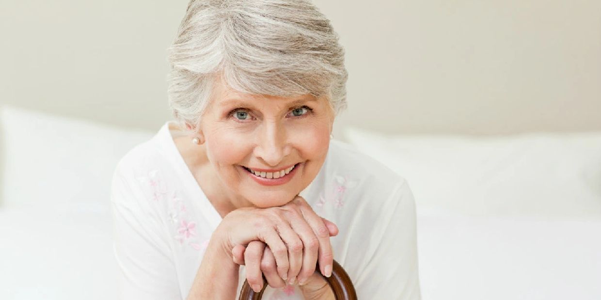 Smiling elderly woman with gray hair rests hands on a cane.