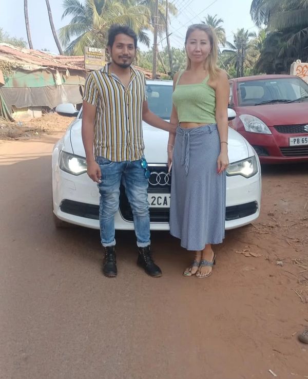 A man and woman standing in front of a white Audi car on a sunny day.