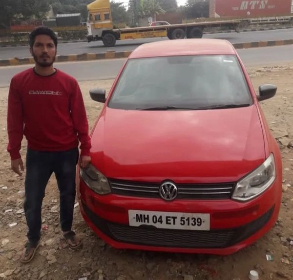 Man in red sweatshirt standing next to a red Volkswagen car.