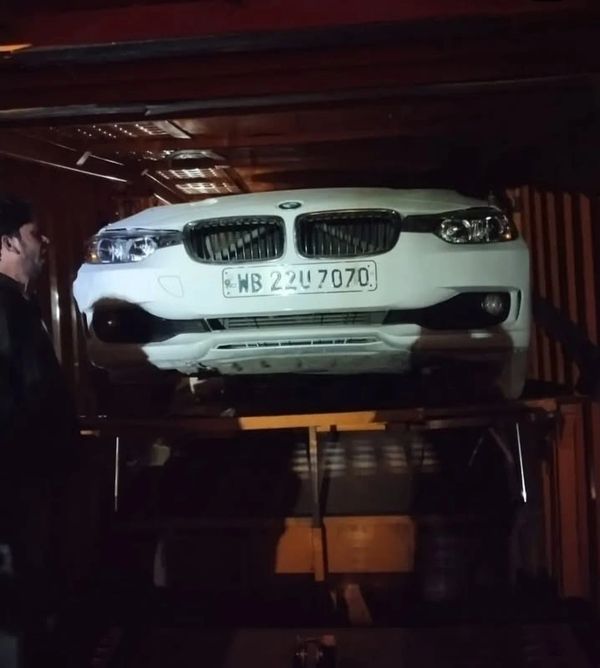 White BMW car inside a dimly lit container with a man nearby.