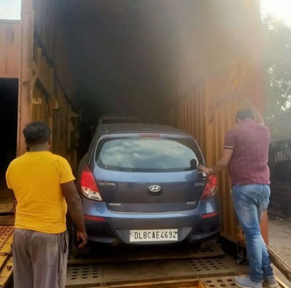 Two men loading a blue Hyundai i20 car into a container.