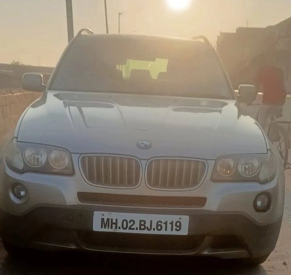 Front view of a silver BMW SUV in sunlight with visible license plate.