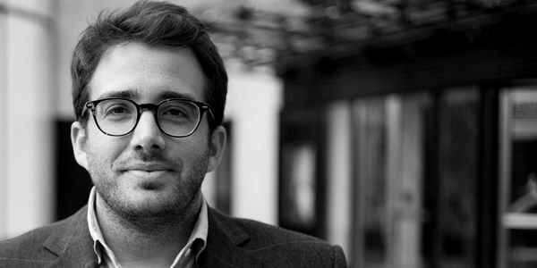 Black and white portrait of a man wearing glasses and a blazer, smiling slightly.