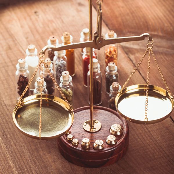 A vintage brass balance scale with small glass spice jars in the background.
