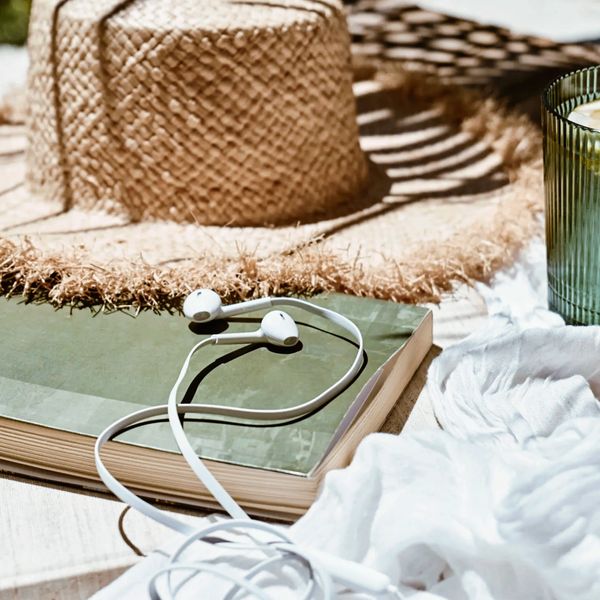 Earphones rest on a closed book beside a straw hat and a candle, suggesting a relaxing day.