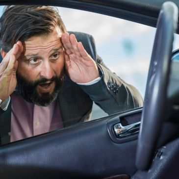 Stressed man looking into a car through an open window.