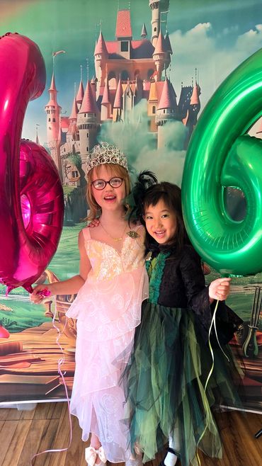 Glinda and Elphaba birthday girls holding their pink and green balloons