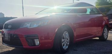 Red Kia car with sunlight glare on the windshield.