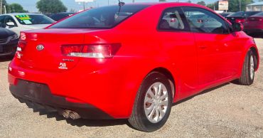 Red Kia coupe parked outdoors on a sunny day.