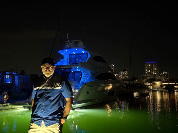 Man standing near a yacht illuminated by colorful lights at night.