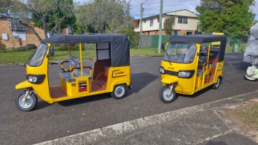 Two yellow LiKONG tuk-tuks parked on a suburban street.