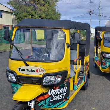 Two colorful yellow tuk tuks parked on a street with clear weather.