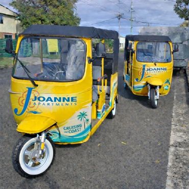 Two yellow auto rickshaws with Joanne Apartments branding parked on a road.
