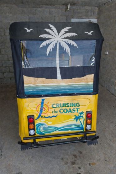Rear view of a yellow tuk-tuk with beach-themed artwork and 'Cruising the Coast' text.