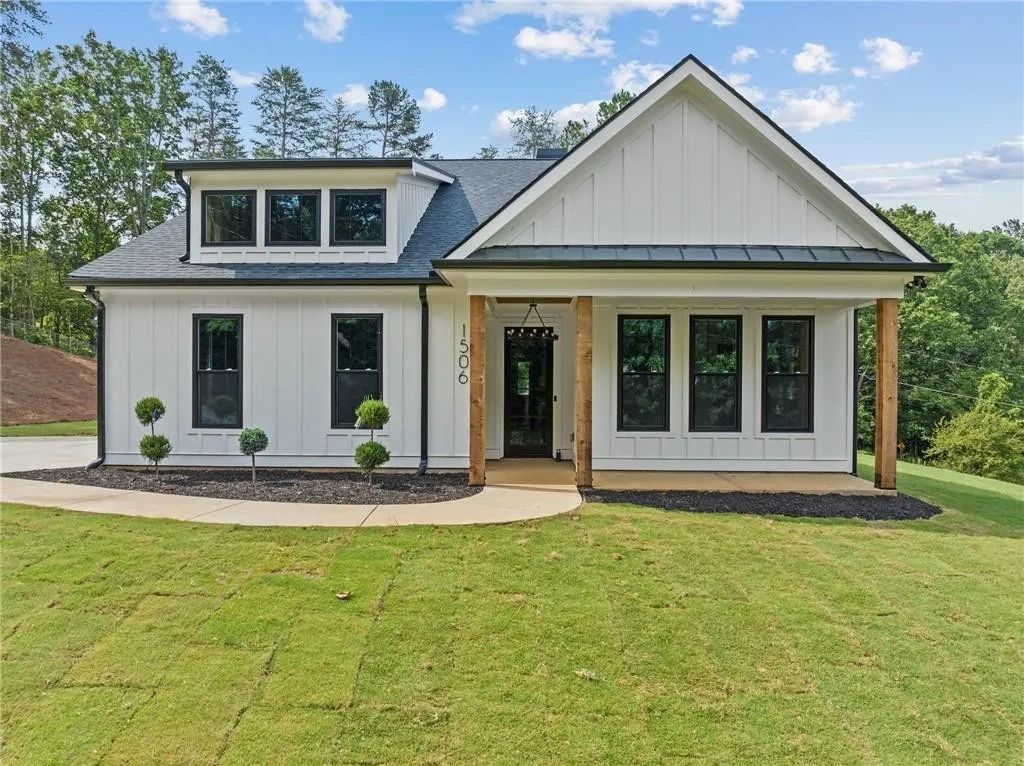 Modern white farmhouse with a manicured lawn and wooden porch columns.