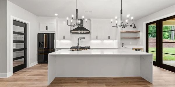 Modern white kitchen with large island, black appliances, and chandeliers.