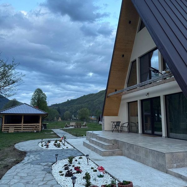 Modern A-frame house with garden and mountain view under cloudy sky.