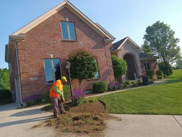 A man doing landscaping work outside a brick house on a sunny day.