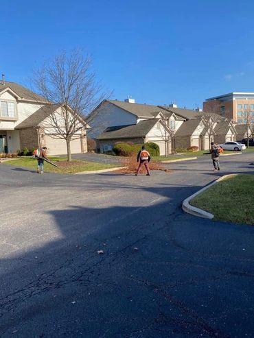 Three people using leaf blowers in a residential neighborhood on a clear day.