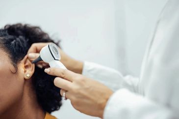 A doctor using an otoscope to examine a young woman's ear for an ENT checkup.