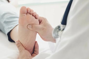 Doctor in a white coat examining and palpating the sole of a patient's foot.