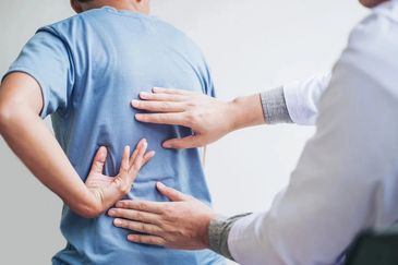 Doctor examining a patient's lower back, symbolizing pain management or chiropractic care.