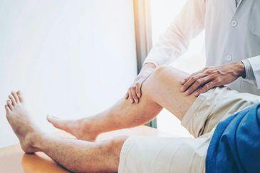 Doctor examining a patient's knee and leg for orthopedic or physical therapy assessment.