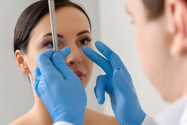 Plastic surgeon in blue gloves examining a woman's facial features for consultation.