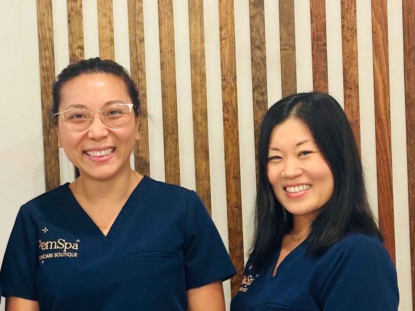 Three PemSpa estheticians smiling in navy uniforms inside the spa with a wood-accented backdrop.