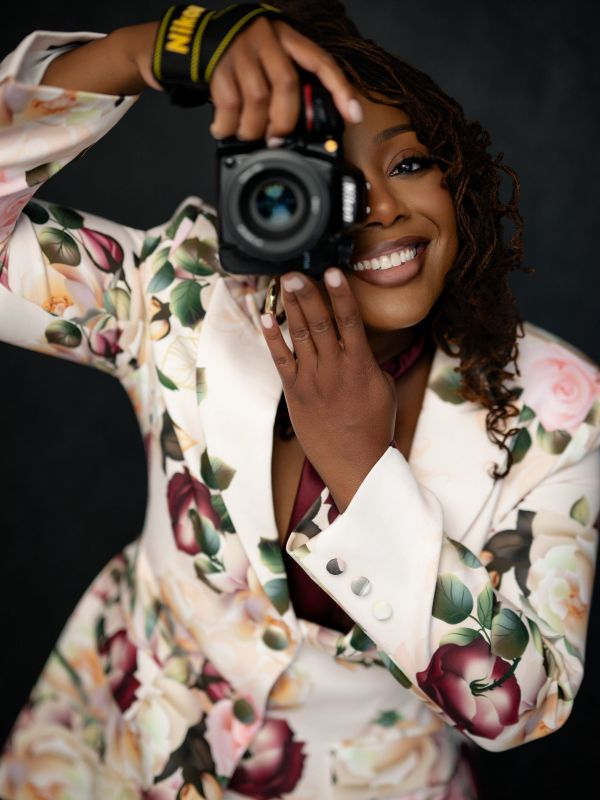 Woman in floral suit taking a photo with a Nikon camera.