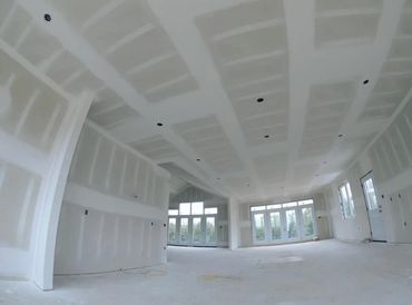 Spacious room under construction with drywall installed and large windows.