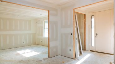 Interior of a home under construction with drywall and a door leaning against the wall.