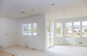 Bright, empty room under construction with large windows and white walls.