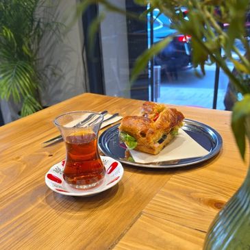 A croissant sandwich and a glass of tea on a wooden table.