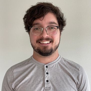 Smiling man with glasses and a beard wearing a light grey henley shirt.