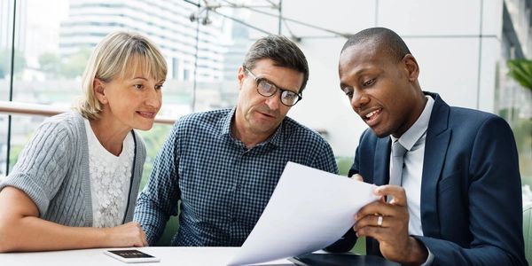 A professional man explains documents to a couple in a modern office.