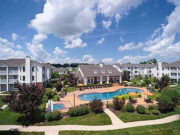 Apartment complex with central pool and clubhouse under a cloudy blue sky.