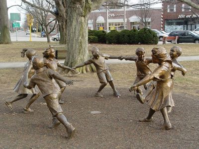 Bronze statues of children playing ring-around-the-rosie outdoors.
