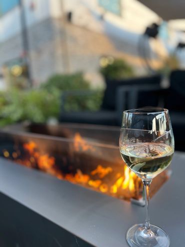 A glass of white wine near a cozy outdoor fire pit.