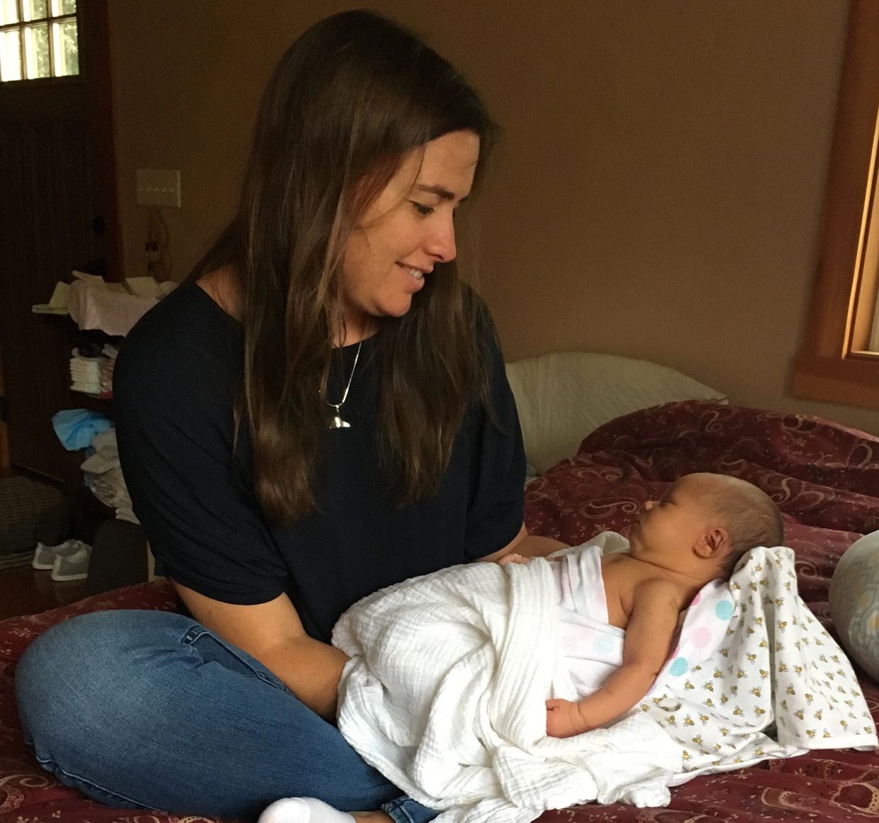 Woman lovingly holding a swaddled newborn baby on a bed.